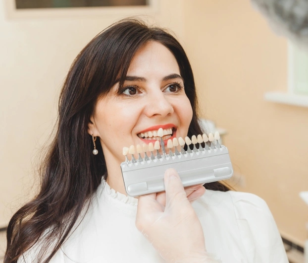 Woman holding dental shade guide showing tooth color options for veneers in Aurora, Illinois.