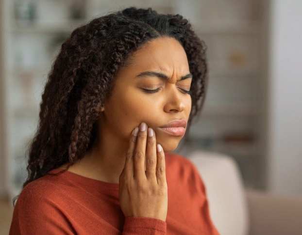 Woman with tooth pain holding cheek at emergency dentist in Aurora, IL.