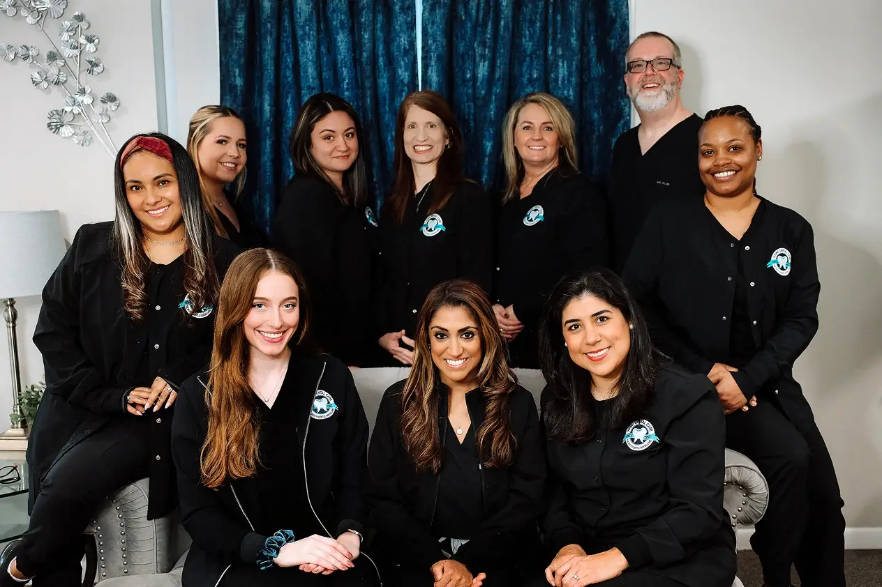 Dental team of 10 professionals in black uniforms smiling together in Aurora office.